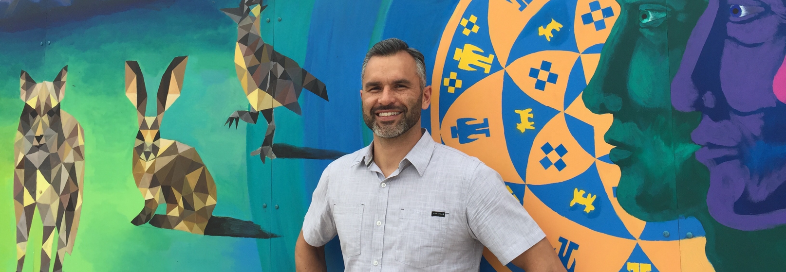 Photograph of Carlos Aguilar in front of a colorful mural